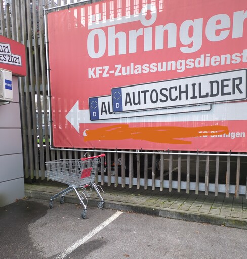 Ein Einkaufswagen steht vor einer Zulassungsstelle.
